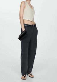 Débardeur court côtelé beige avec encolure dégagée, associé à un pantalon cargo noir taille haute avec poches et ceinture, et une pochette noire.