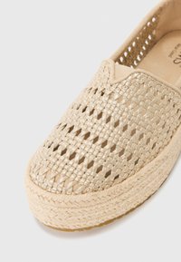 Beige pletené slip-on boty s texturovaným vzorem, s juty provázkovou podrážkou a jemným metalickým leskem. Uzavřený špičkový design.