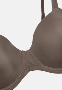 Ljusbrun vadderad bh med slät tyg, undertrådsstöd och justerbara axelband. Har rundade kupor och sömmar längs kanterna.