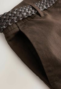 Pantalon marron foncé avec une ceinture en cuir marron foncé tressée passée dans la boucle de la ceinture.