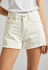 Shorts de mezclilla blanca con dobladillo deshilachado, con cierre de botón frontal, trabillas para cinturón y bolsillos laterales. Textura suave y diseño casual.