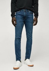 Kapeat siniset farkut, jotka on valmistettu denimistä. Farkuissa on klassinen viiden taskun malli ja hienovarainen haalistuma, yhdistettynä valkoisiin tennareihin.