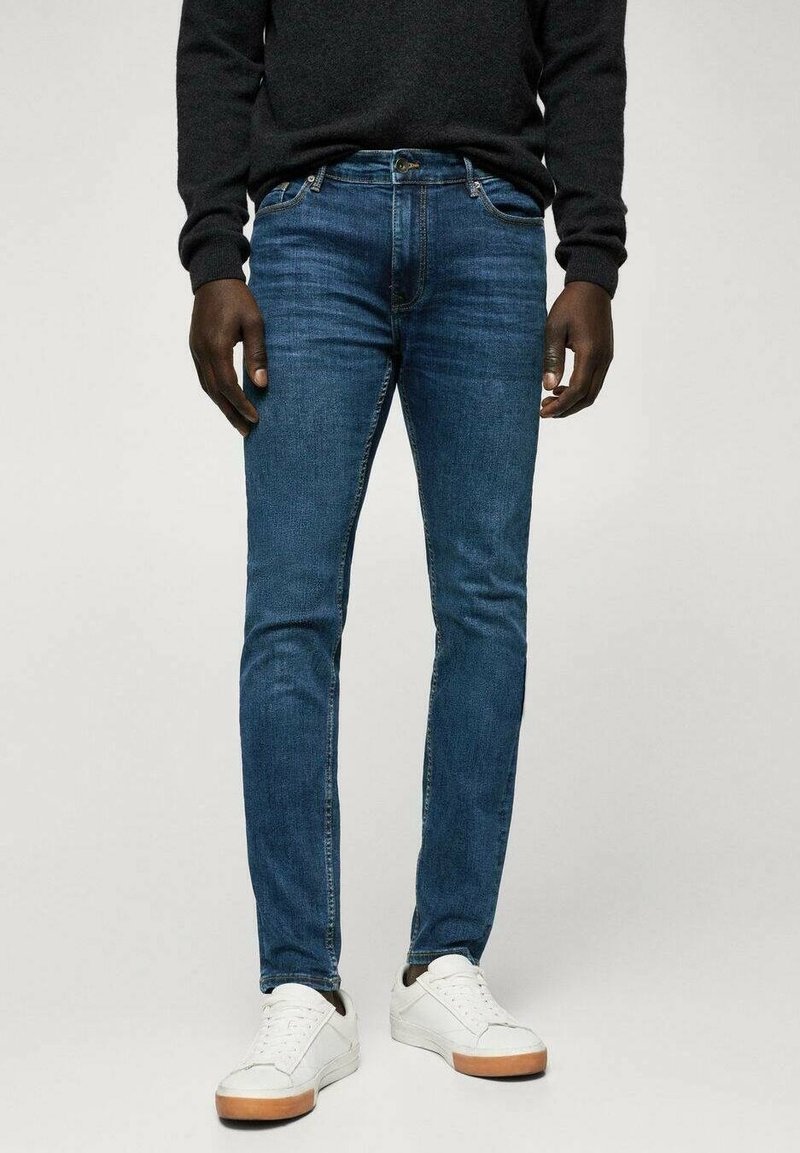 Kapeat siniset farkut, jotka on valmistettu denimistä. Farkuissa on klassinen viiden taskun malli ja hienovarainen haalistuma, yhdistettynä valkoisiin tennareihin.