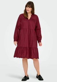 Burgundy cotton dress with long sleeves, a tiered design, and embroidered accents at the hem. Features a v-neckline and relaxed fit.
