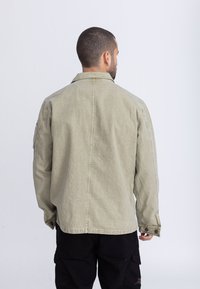 Olivgrüne Denimjacke mit lockerem Schnitt, geknöpften Ärmeln und geradem Rückennaht. Bietet minimale Details und eine weiche Textur.