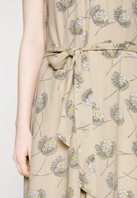 Μπεζ φόρεμα με λουλουδάτο μοτίβο σε παστέλ αποχρώσεις, με ζωνάκι στη μέση, απαλή υφή και ρέουσα σχεδίαση.