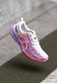 Running shoe with a white mesh upper featuring red and purple abstract patterns, a purple sole and lace-up design, designed for mobility and comfort.