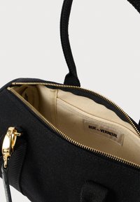 Μαύρη τσάντα από ύφασμα με χρυσό φερμουάρ, εσωτερική τσέπη σε μπεζ απόχρωση με την επιγραφή "RUE de VERNEUIL", και μαύρος ιμάντας με χρυσό κούμπωμα.