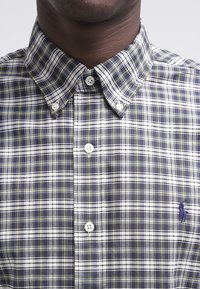 Camisa a cuadros en tonos de púrpura, blanco y verde. Cuenta con un collar tipo button-down, botones blancos y un pequeño logo bordado. Tela de algodón.