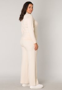 Beige getailleerde lange mouw top en ruime broek van zachte stof. De outfit heeft een soepele textuur en een minimalistisch design. Witte schoenen maken de look compleet.