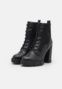 Black ankle boots featuring a mix of leather and knit materials, a rounded toe, high block heel, and front lacing design.