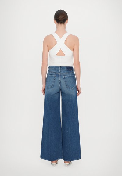 White crossback top with a cutout detail paired with high-waisted, wide-leg blue denim jeans. Smooth fabric with a light wash gradient.