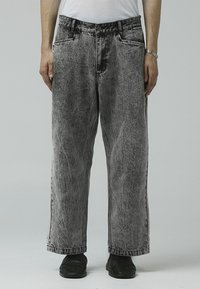Vide ben, falmet sorte denim jeans med teksturert overflate. Har frontlommer og rett skår. Bæres med sorte sko.