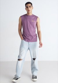 Purple sleeveless shirt, light blue ripped jeans, and black sneakers. The shirt features a small logo detail on the chest.
