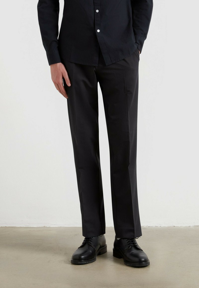 Schwarze Anzughosen mit geradem Schnitt, glattem Stoff und seitlichen Taschen, kombiniert mit eleganten schwarzen Schnürschuhen.