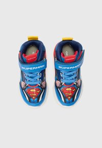 Blaue und rote Turnschuhe mit einem Superman-Design, ausgestattet mit einem Riemenverschluss, strukturiertem Stoff und grafischen Akzenten des Superhelden-Logos.
