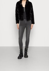 Black faux fur jacket with a zip closure, gray slim-fit jeans, and black chunky ankle boots with buckle accents. Smooth texture overall.