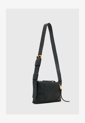 Fekete bőr oldaltáska széles, állítható pánttal, arany csattal, elülső zsebbel és arany cipzárhúzóval világosszürke háttéren.