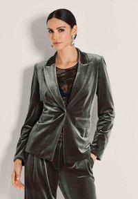 Samtiger dunkelgrüner Blazer mit einer Ein-Knopf-Verschluss, gekerbten Revers und zwei vorderen Taschen, kombiniert mit einem schwarzen Spitzentop.