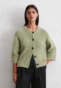 Grüner, flauschiger Cardigan mit Rundhalsausschnitt und Dreiviertelärmeln, der fünf dunkle Knöpfe auf der Vorderseite aufweist. Strukturierter Stoff.