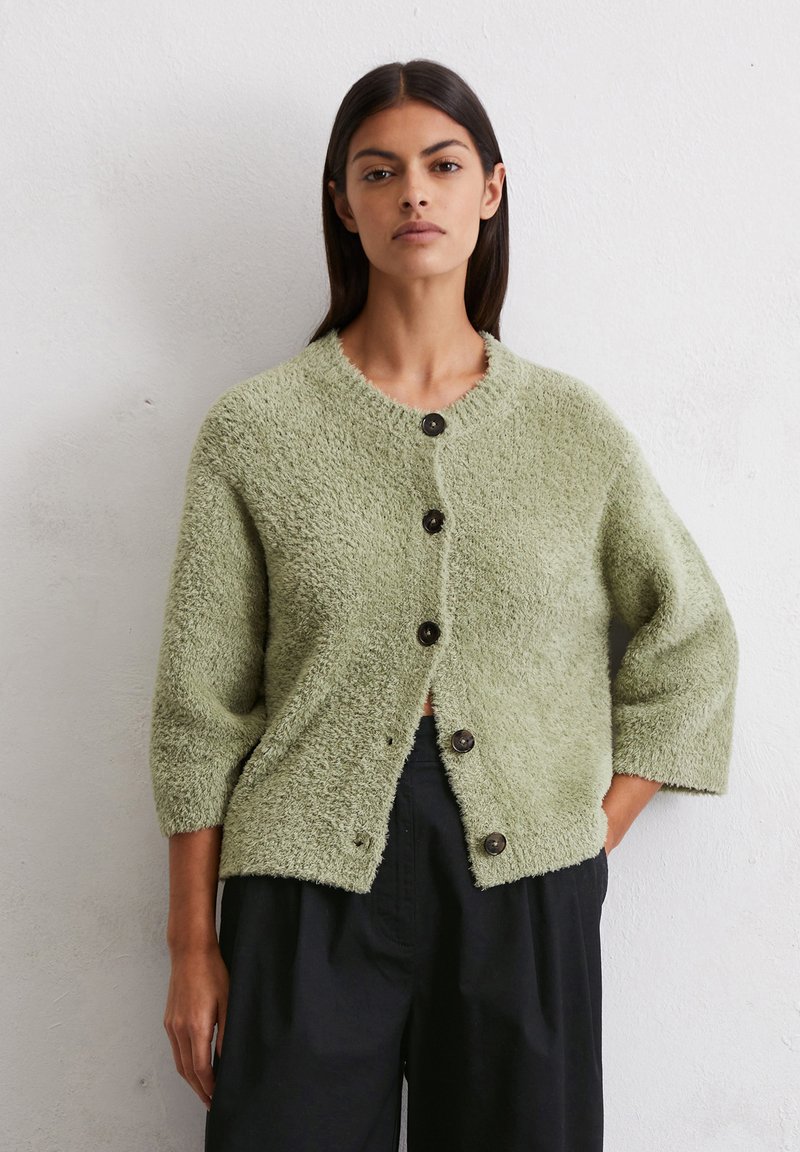 Grüner, flauschiger Cardigan mit Rundhalsausschnitt und Dreiviertelärmeln, der fünf dunkle Knöpfe auf der Vorderseite aufweist. Strukturierter Stoff.