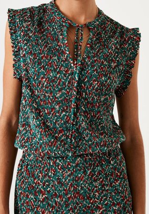 Hihaton laskostettu paita röyhelöreunuksilla ja solmittavalla pääntiellä, väriltään teal, punainen, valkoinen ja musta abstraktissa kuviossa, pidettynä yhdessä vastaavan laskostetun hameen kanssa.