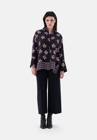 Black patterned silk shirt with white floral designs, featuring a classic collar and a curved hem, paired with wide-leg black trousers.