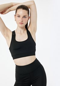 Schwarzer Sport-BH mit Rundhalsausschnitt und Racerback-Design. Hat eine glatte Textur und minimale Nähte, kombiniert mit hochtaillierten schwarzen Leggings.