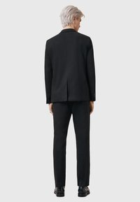 Zwart op maat gemaakt pak met een twee-delig ontwerp, voorzien van een enkele split aan de achterkant en slim-fit broeken, gecombineerd met zwarte schoenen.