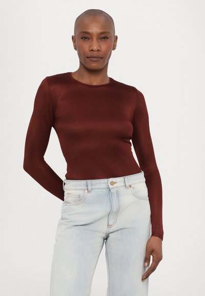 Bordeauxfarbenes Langarmoberteil mit gerippter Textur, kombiniert mit hellblauen, hochtaillierten Jeans im klassischen Fünf-Taschen-Design und einem Metallknopf.
