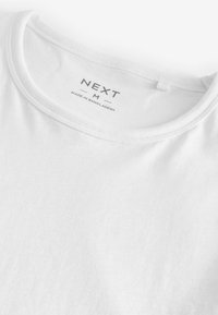 T-shirt bianca in cotone con scollo rotondo e tessuto leggero e liscio. L'etichetta riporta "NEXT M", indicando la taglia e il paese di origine.