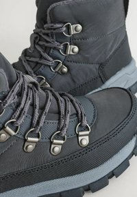 Ciemnoszare buty trekkingowe z teksturowaną cholewką, metalowymi oczkami, solidnymi sznurowadłami oraz wytrzymałą gumową podeszwą zapewniającą przyczepność.