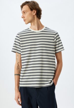 Camiseta de manga corta a rayas en crema con líneas marinas, escote redondo, corte relajado y textura de tela suave. Presenta acentos de costura sutiles.
