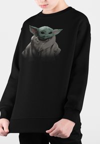 Svart sweatshirt med en grafik av en grön karaktär med stora öron, klädd i en kappa. Materialet verkar mjukt med en lös passform.