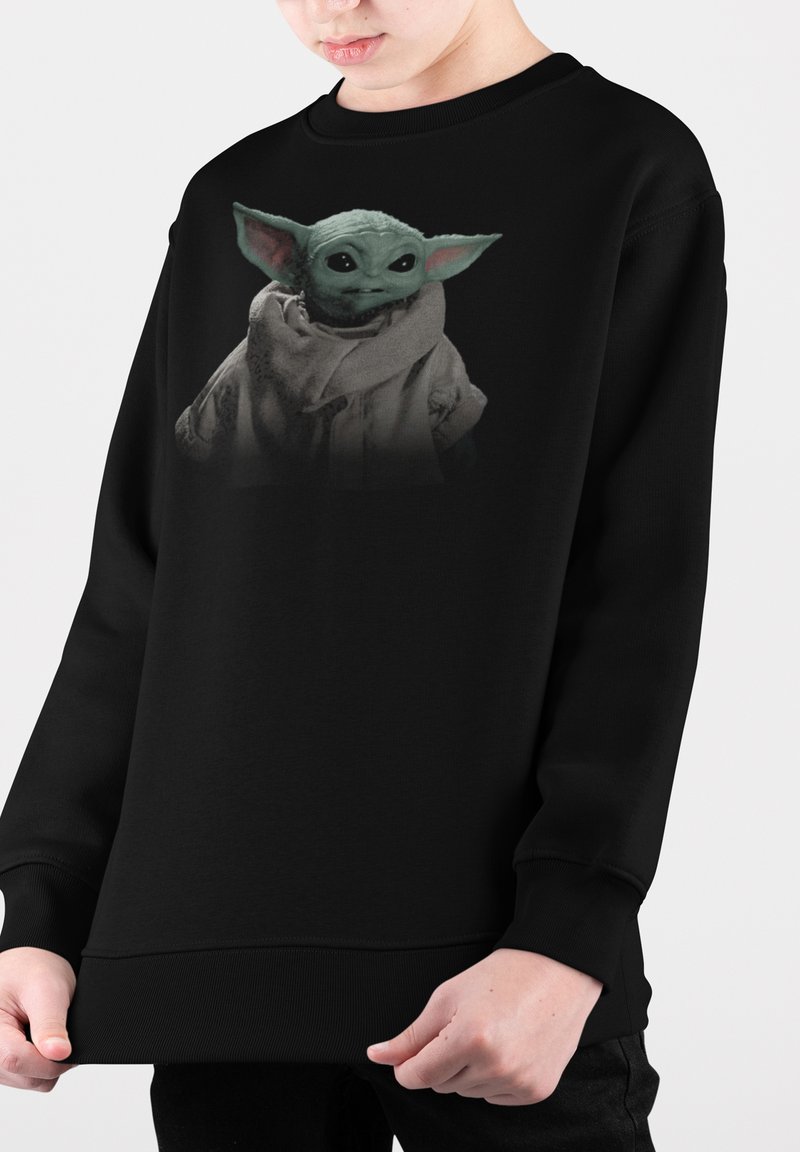 Svart sweatshirt med en grafik av en grön karaktär med stora öron, klädd i en kappa. Materialet verkar mjukt med en lös passform.