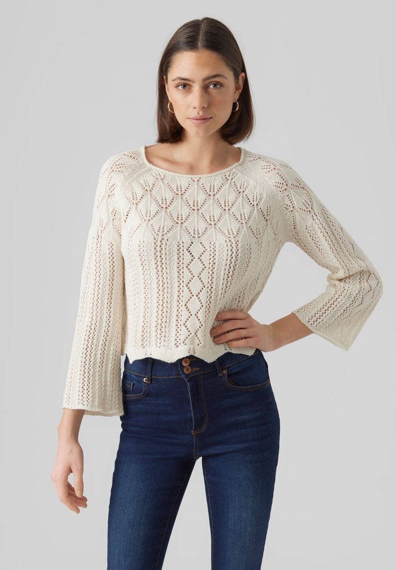 Maglione bianco a maglia con vestibilità comoda, maniche a tre quarti e dettagli a motivo romboidale, abbinato a jeans blu scuro a vita alta.
