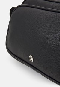 Svart teksturert lærveske med en glatt finish, med en fremtredende sølvlogo og elegante, avrundede kanter. Stilige designdetaljer.
