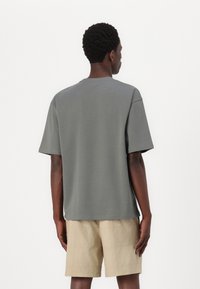 Graues Baumwoll-T-Shirt mit lockerer Passform und kurzen Ärmeln, kombiniert mit beigen Leinen-Shorts. Der Stoff hat eine glatte Textur.