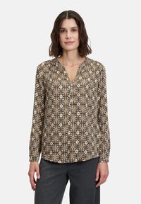 Langärmlige Bluse aus gemustertem Stoff mit floralen Motiven in Beige, Schwarz und Braun, mit einem V-Ausschnitt und einem Knopf-Accessoire an der Vorderseite.