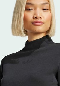 Svart höghalssweatshirt i mjukt material, med en subtil, präglad logga på bröstet. Slät textur och figursydd design.