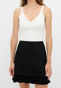 Bílý přiléhavý tílko s výstřihem do V a tenkými ramínky spárované s černou skládací sukní s volánovým lemem.