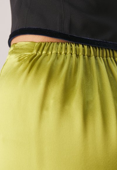 Groene satijnen stof met een gladde textuur en een elastische tailleband, gecombineerd met een zwarte top met een fluwelen rand aan de onderkant.