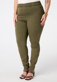Olijfgroene skinny jeans met een elastische tailleband, voorzien van zijzakken en een gladde, gestructureerde stof. Draag ze met zwarte sleehakken.