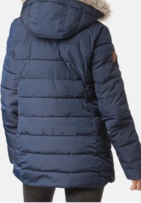 Chaqueta tipo puffer en color navy con costuras horizontales, capucha forrada de pelo y un parche con un logo redondo en el brazo izquierdo. Tejido exterior liso y brillante.