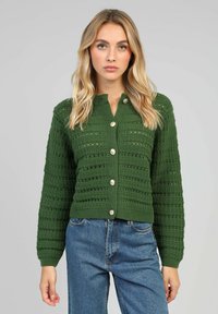 Cardigan tricoté vert avec un motif texturé, dotée d'un design cropped, manches longues et grands boutons sur le devant.