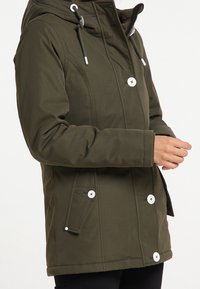 Veste imperméable vert olive avec capuche, boutons à l'avant et poches sur les côtés. Texture lisse avec des accents de boutons blancs et des détails cousus.