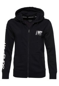 Sudadera con cremallera negra hecha de una mezcla de algodón, con capucha ajustable, bolsillos frontales y texto del logo en blanco a lo largo de la manga.
