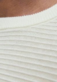 Pull en maille beige clair avec texture côtelée et col rond. Le tissu est doux et a une finition lisse.
