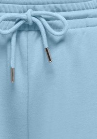 Tissu bleu clair avec un cordon noué en nœud orné d'embouts en métal aux extrémités, probablement une partie de la ceinture d'un vêtement.
