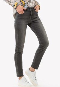 Jeans de denim gris con un corte ajustado, cinco bolsillos y un desvanecimiento sutil, combinados con zapatillas blancas. La tela tiene una textura suave.